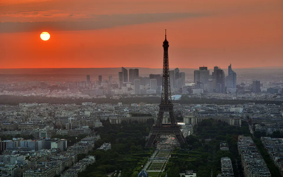 París desde el aire al atardecer, con la Torre Eiffel recortada contra un cielo naranja y los rascacielos de La Défense al fondo