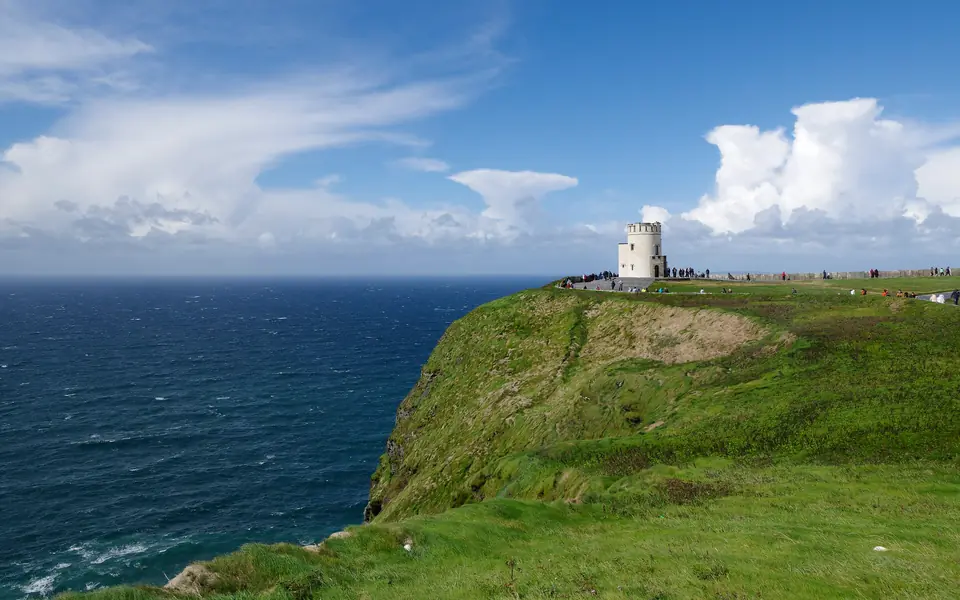 Los acantilados de Moher desde el prado: la pared verde cayendo a plomo sobre el Atlántico y la torre de O'Brien recortada contra las nubes