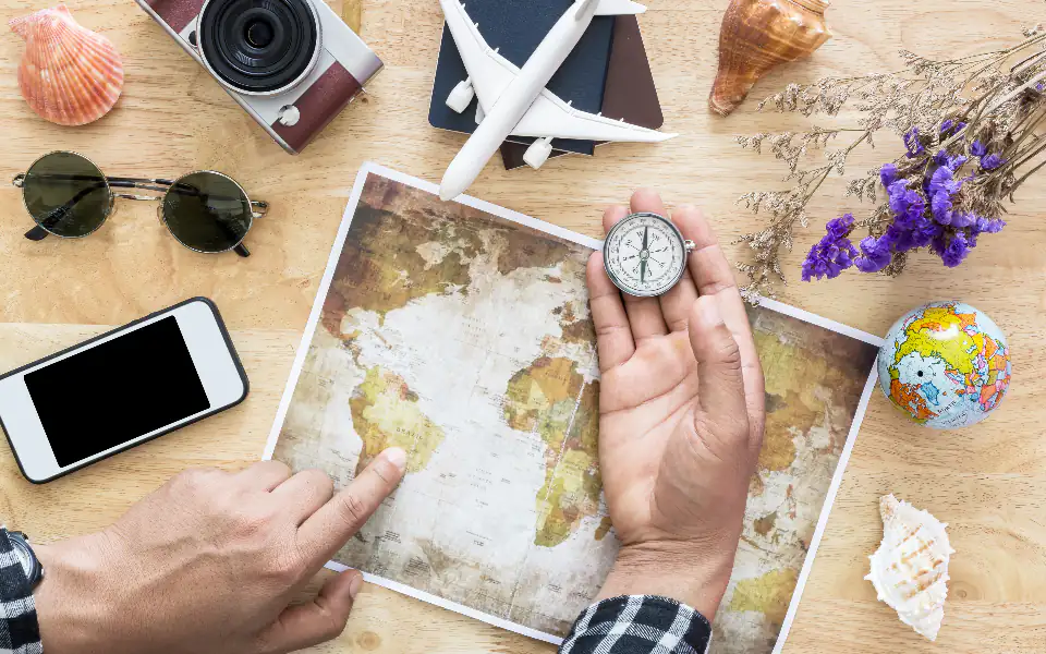 La mesa entera de planear un viaje: el mapa del mundo con una mano señalando, una brújula, un avión de juguete sobre un pasaporte, gafas de sol y un globo terráqueo