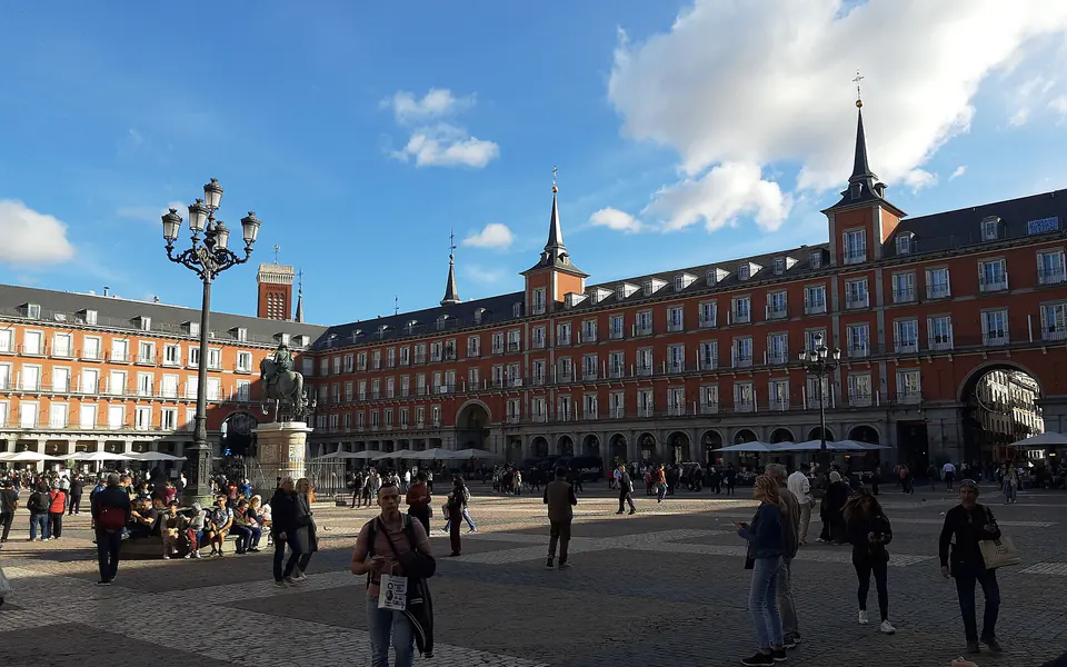 La Plaza Mayor de Madrid a media tarde: las fachadas rojas con sus buhardillas, la estatua de Felipe III y gente cruzando el empedrado