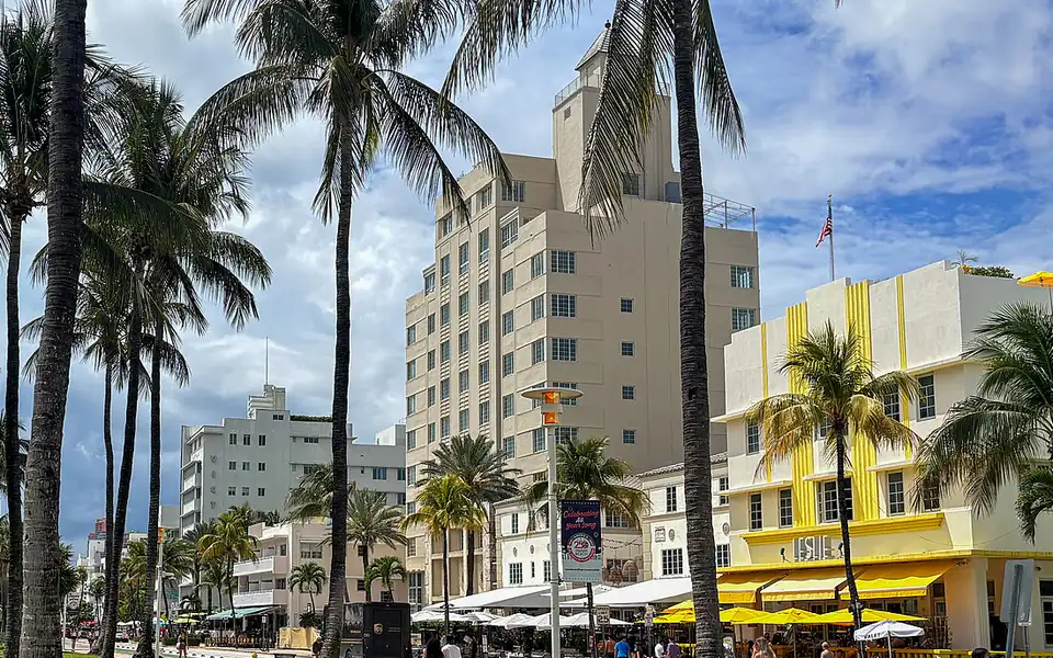 Ocean Drive visto entre las palmeras de Lummus Park, con los hoteles art decó blancos y amarillos y sus toldos en la acera