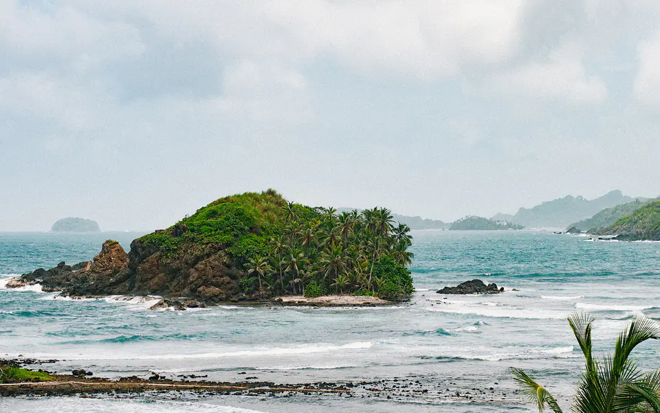Un islote cubierto de palmeras frente a la costa caribeña de Panamá, con el oleaje rompiendo en las rocas